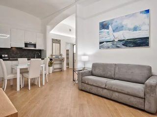 Bright and modern apartment living space with white furniture, a red sofa, and a large painting of a sailboat.